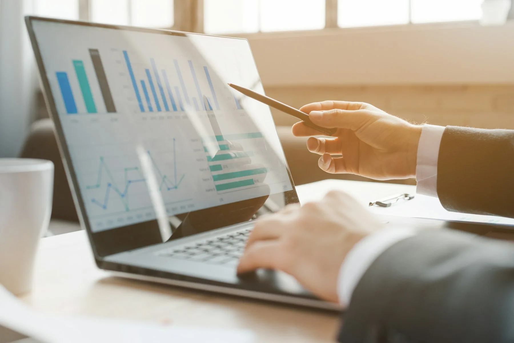 Hands reviewing illustrative business charts on a laptop.