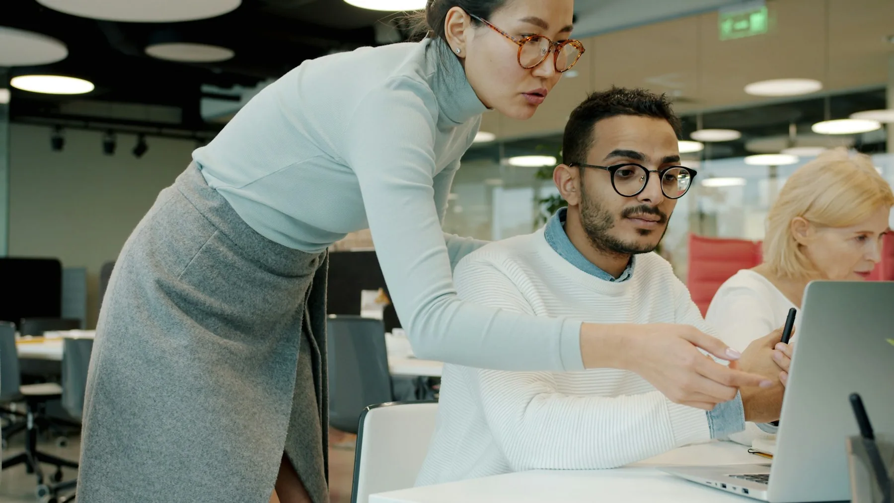 Colleagues coordinating a task at a laptop in an office.