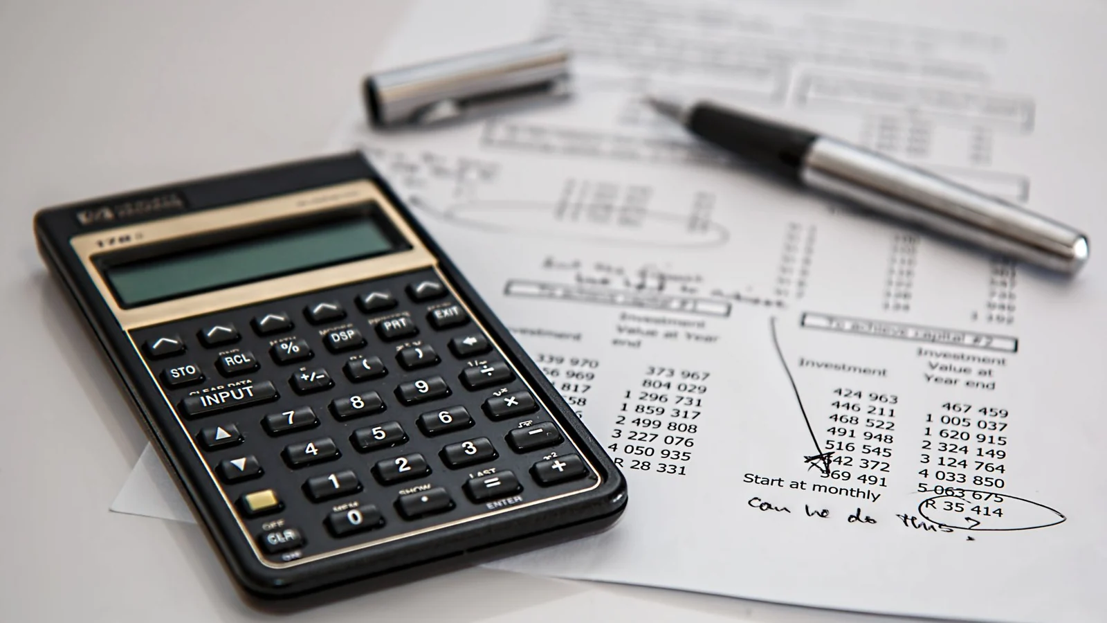 A calculator, pen and printed financial figures on a desk.