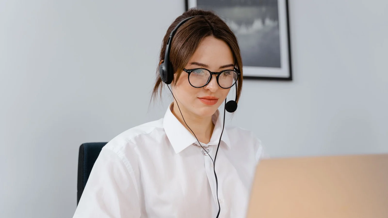 A headset-wearing office worker handling a call beside a laptop.