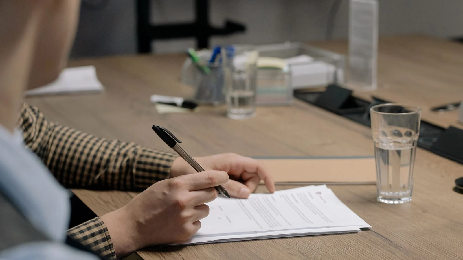 Hands reviewing a paper document and marking it with a pen at a shared desk.