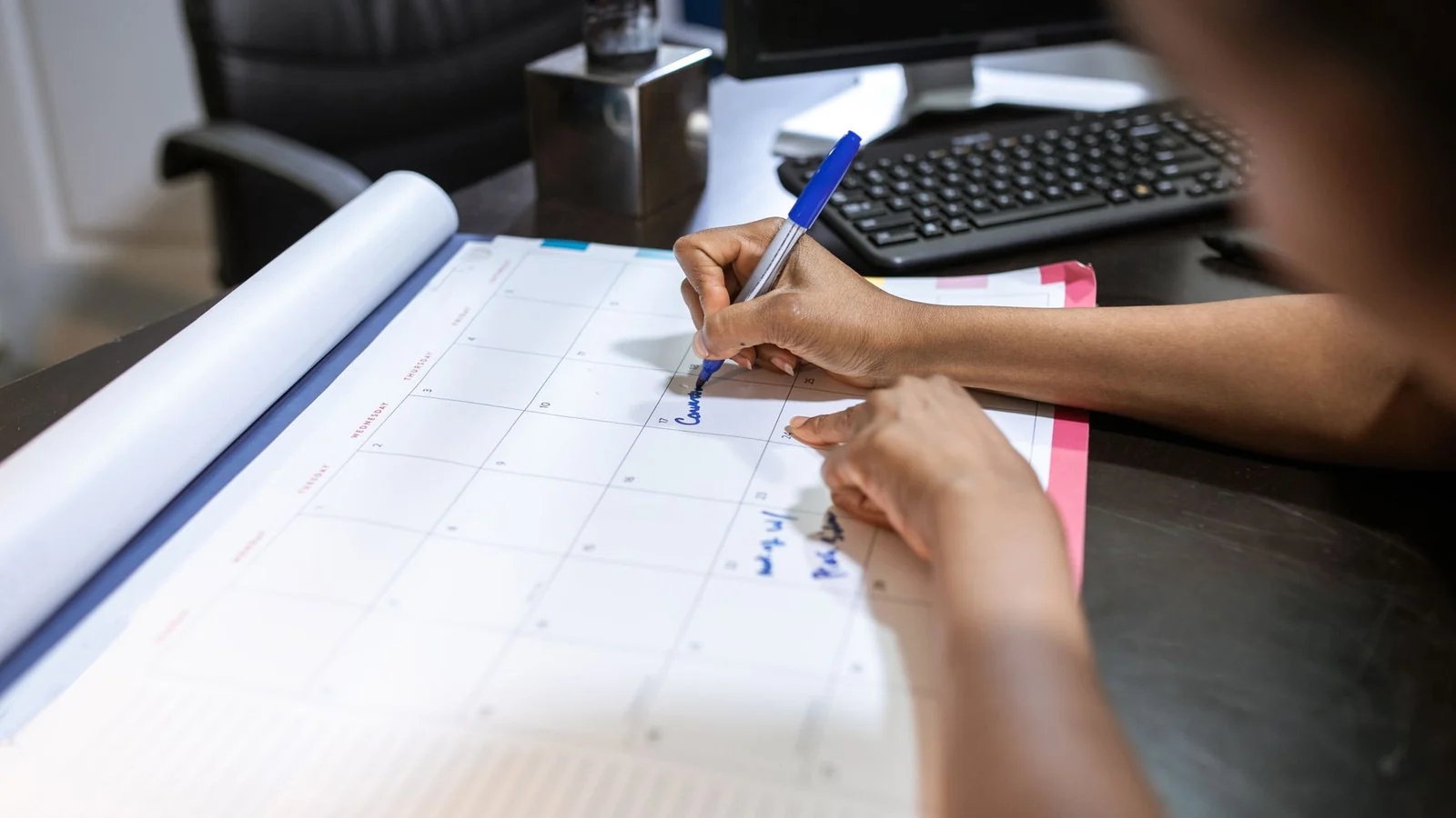 A person marking a large desk calendar with a blue pen.